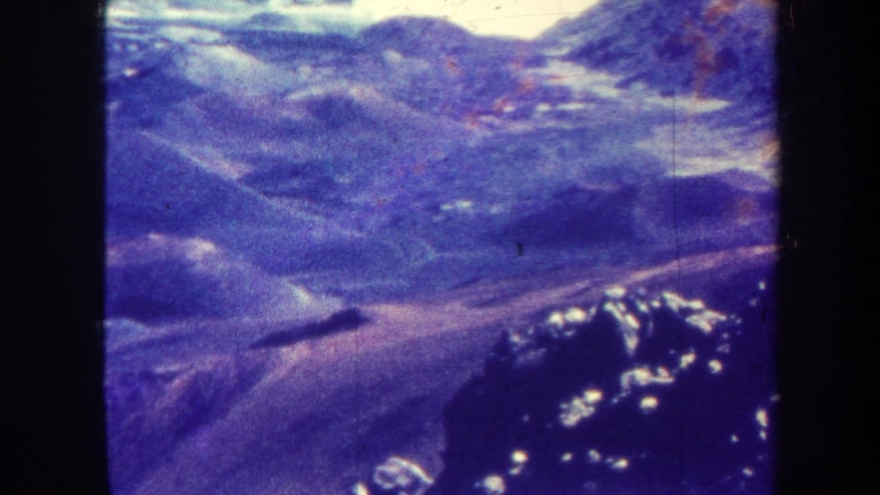 Aerial terrain frame with blue-purple hills, valleys, and dark vertical film borders.
