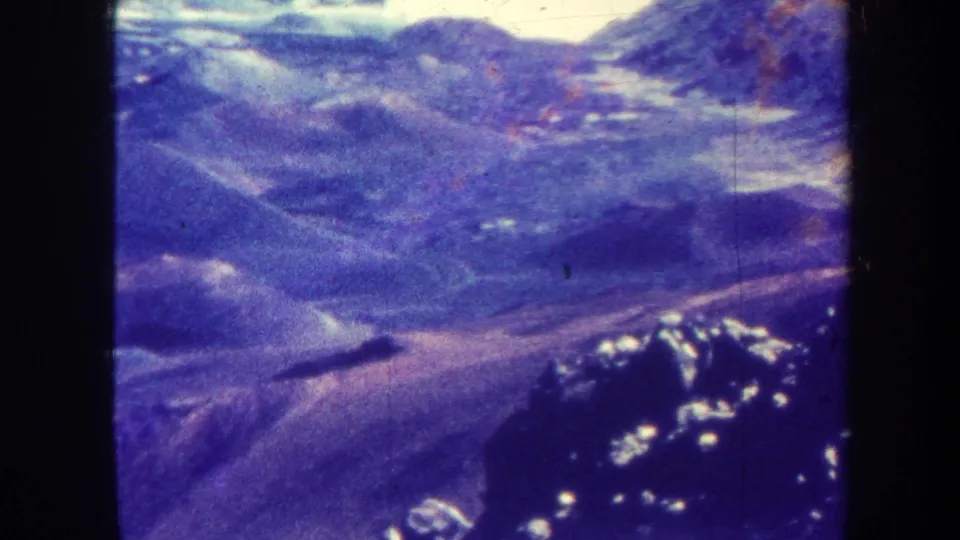 1967 Hawaii home-movie frame with an aerial view of volcanic-looking ridges and valleys, tinted blue-purple by aged film color.