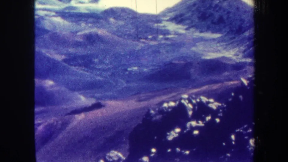 1967 Hawaii 8mm still showing a soft aerial view across hills and valley forms, with bright highlights, grain, and a pronounced purple tint.