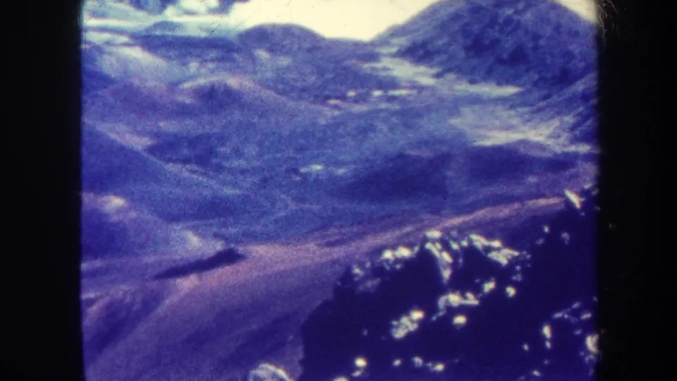 1967 Hawaii home-movie frame showing rugged hills, dark ridges, and valley contours from an aerial viewpoint, with aged 8mm color shift.