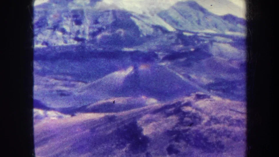 1967 8mm home-movie frame, metadata-labeled Honolulu, showing an aerial view of distant mountain ridges with snow-bright peaks and purple-blue film shift.