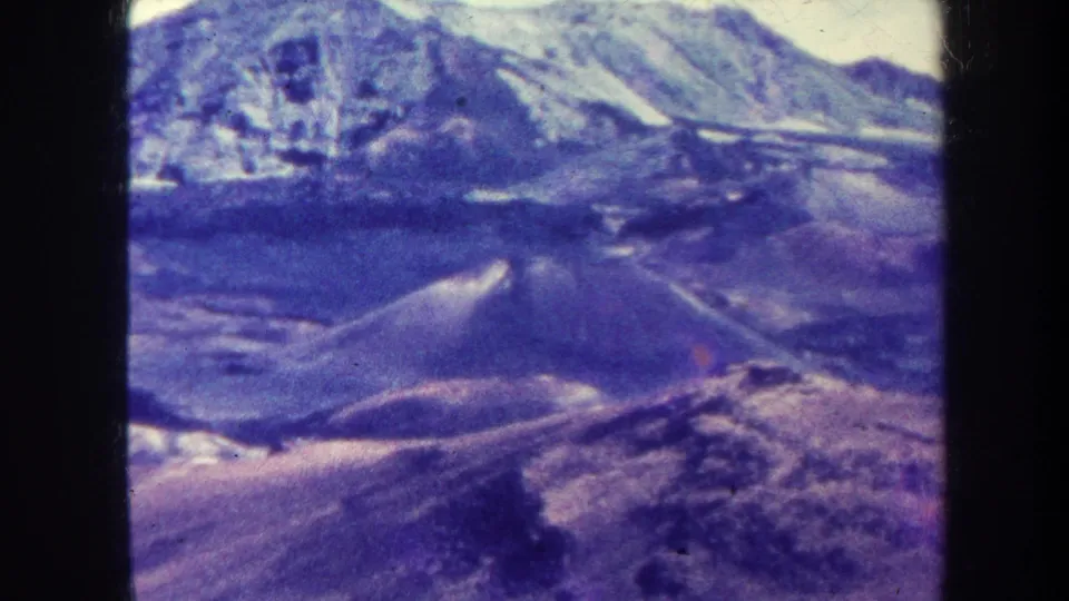 Final 1967 8mm frame holds on the aerial mountain range, with snow-bright high areas, rugged dark slopes, and visible film gate borders.