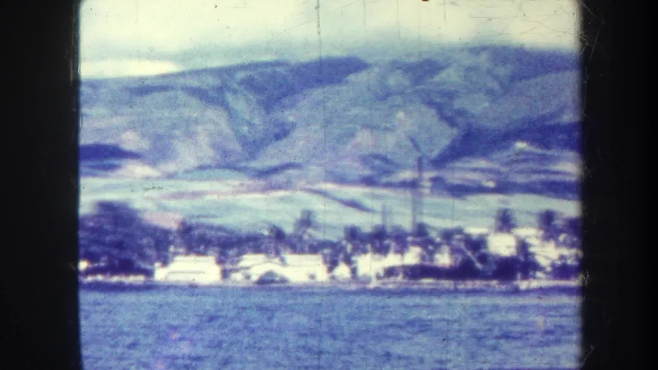 Faded 8mm Honolulu-area landscape with calm water in front of white shoreline buildings, palms, and a broad mountain backdrop.