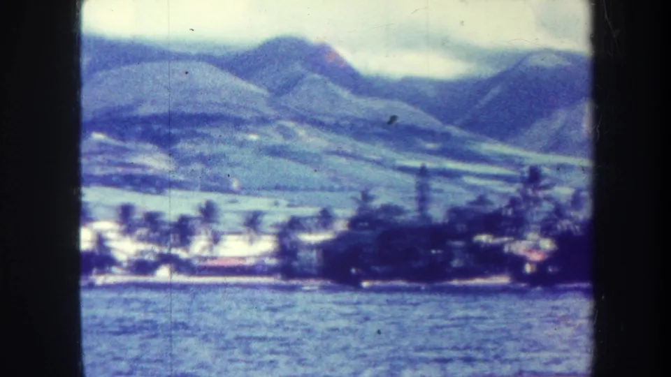 Soft 1967 Honolulu frame of water in the foreground, a palm-dotted shore, low structures, and green mountains behind.