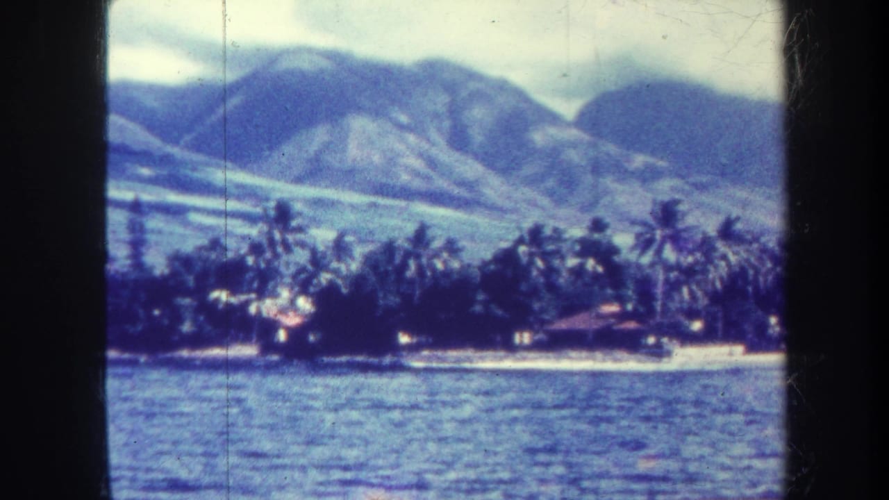Distant beach, palms and mountains viewed over rippled ocean water.