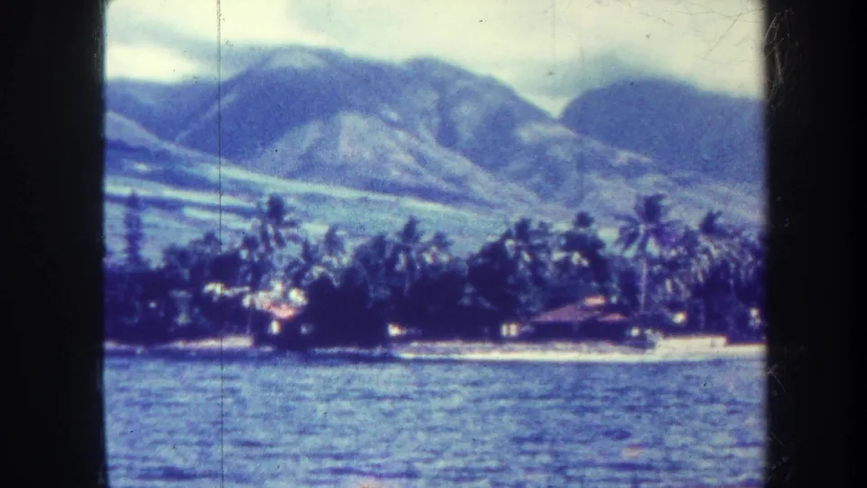 1967 Honolulu shoreline vista with rippled ocean in front, palms and low buildings along the beach, and mountains beyond.