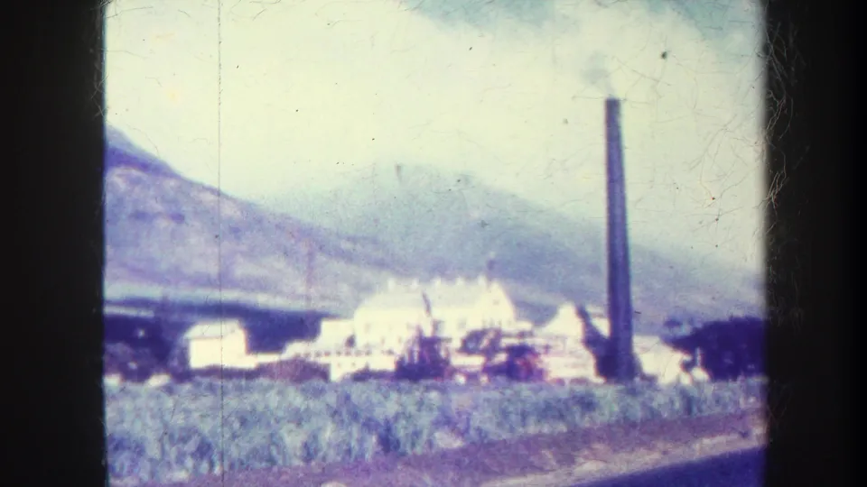 1967 Honolulu frame of a factory complex and tall smokestack across crop fields, with mountains and 8mm gate edges visible.