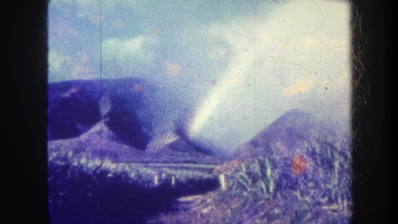 Rainbow over distant mountains with blue sky, clouds and vegetation in the foreground.