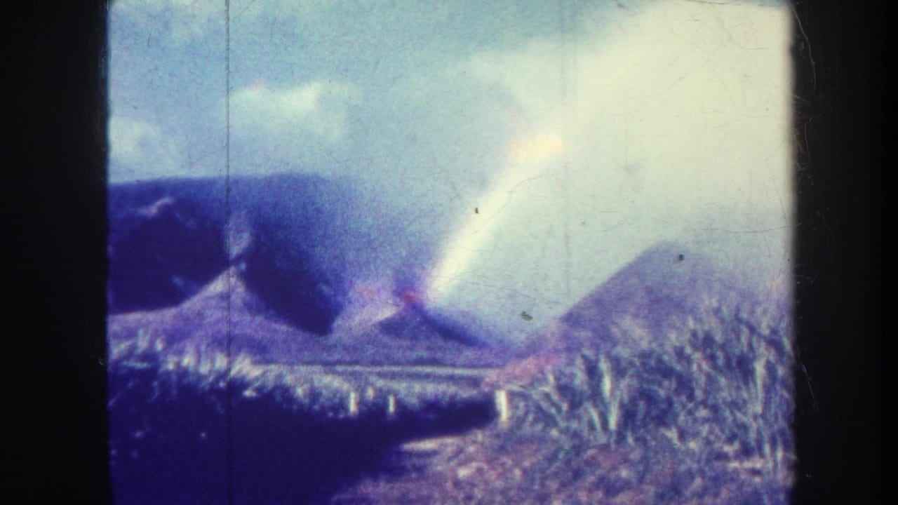 Pale rainbow and clouds above mountain ridges with dense vegetation below.