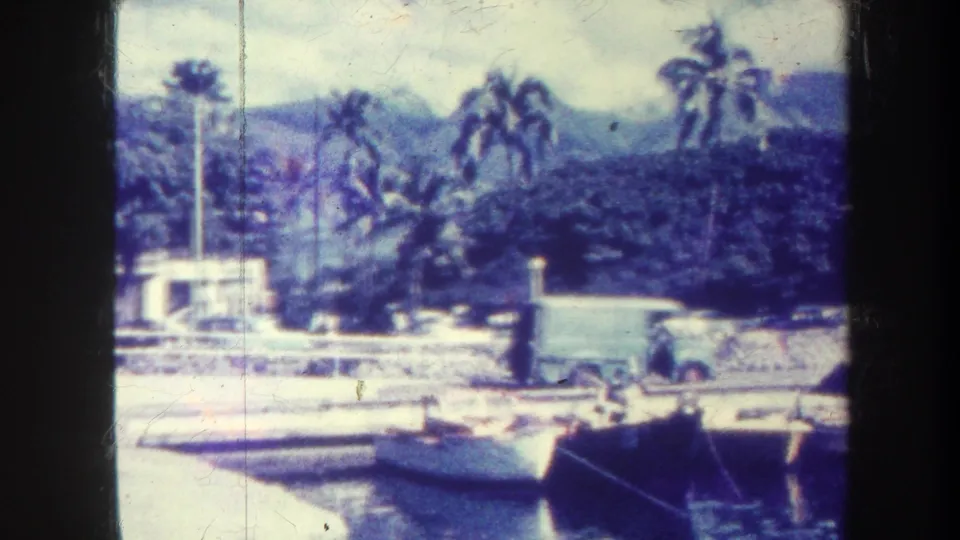Honolulu marina scene from 1967 showing docked boats, a pier, a white van, palm trees, and hazy mountains behind the shoreline.