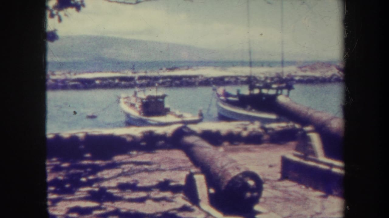 Harbor scene with old cannons in the foreground and small boats behind a breakwater.