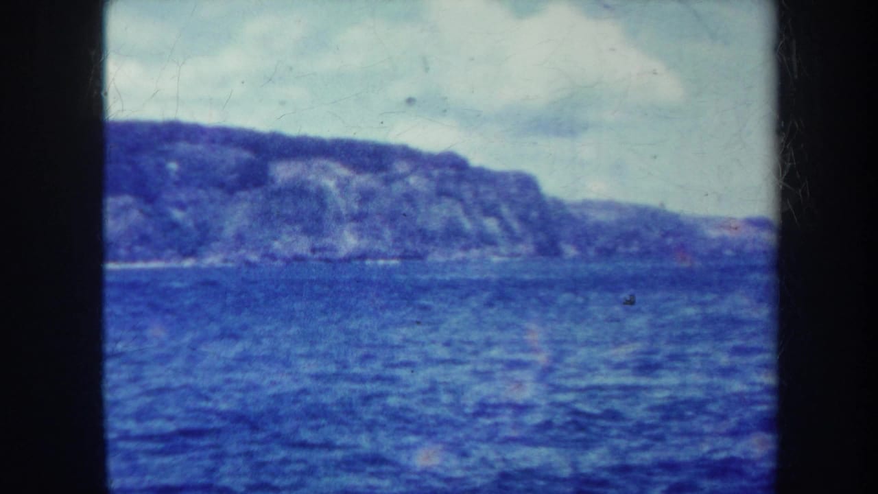 Blue ocean with a rugged tree-covered hill beneath a cloudy sky.