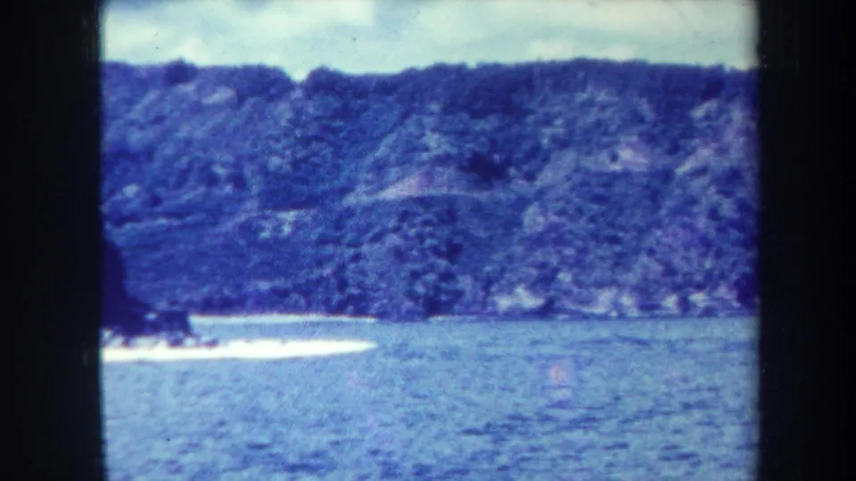 1967 Honolulu-area 8mm frame with a broad water surface, distant wooded ridge, and narrow bright shoreline.