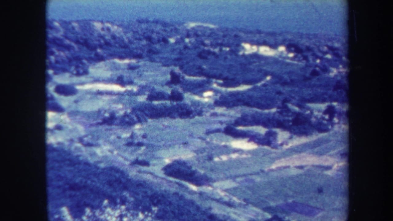 Elevated view over green hills, fields, roads, and scattered light structures.