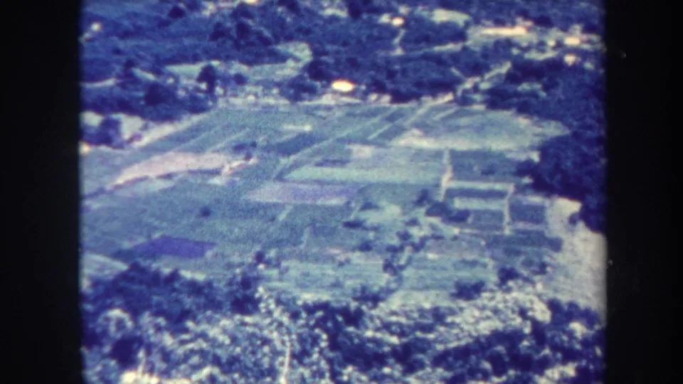 1967 Honolulu aerial home-movie frame with fields, dense trees, and small structures visible below.