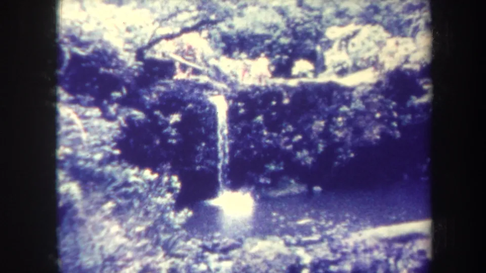 1967 Honolulu 8mm waterfall view with dense greenery, falling water, and a splash in the pool below.