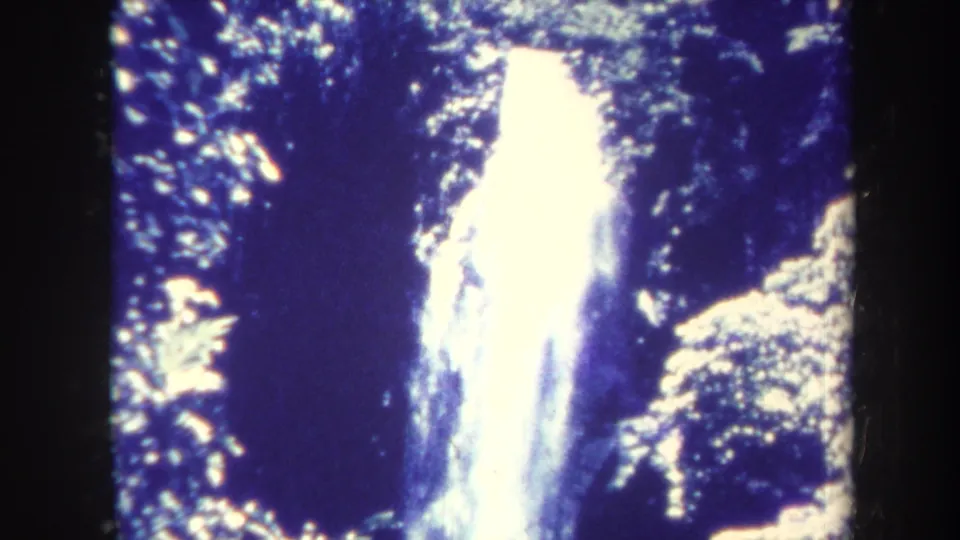 Closer 8mm frame of the Honolulu waterfall, with overexposed white water surrounded by shaded tropical vegetation.
