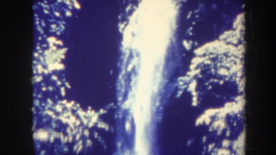 Home-movie close-up of a vertical waterfall in Honolulu, with soft focus, heavy contrast, and surrounding tropical leaves.