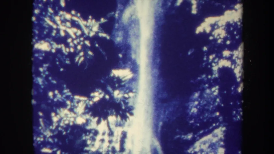 1967 Hawaii travel frame showing a bright waterfall column through dark tropical plants, with blue-purple 8mm color drift.
