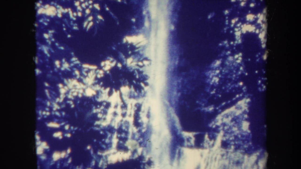 Tall waterfall descending through dark tropical foliage and rock.