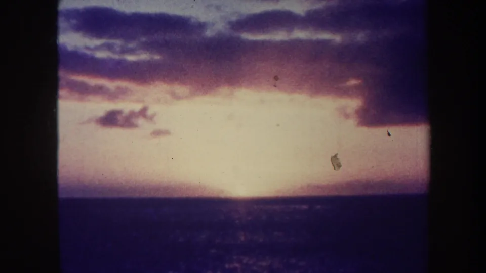 1967 Honolulu 8mm frame of an ocean sunset, with dark water below a bright horizon and purple-pink clouds across the sky.