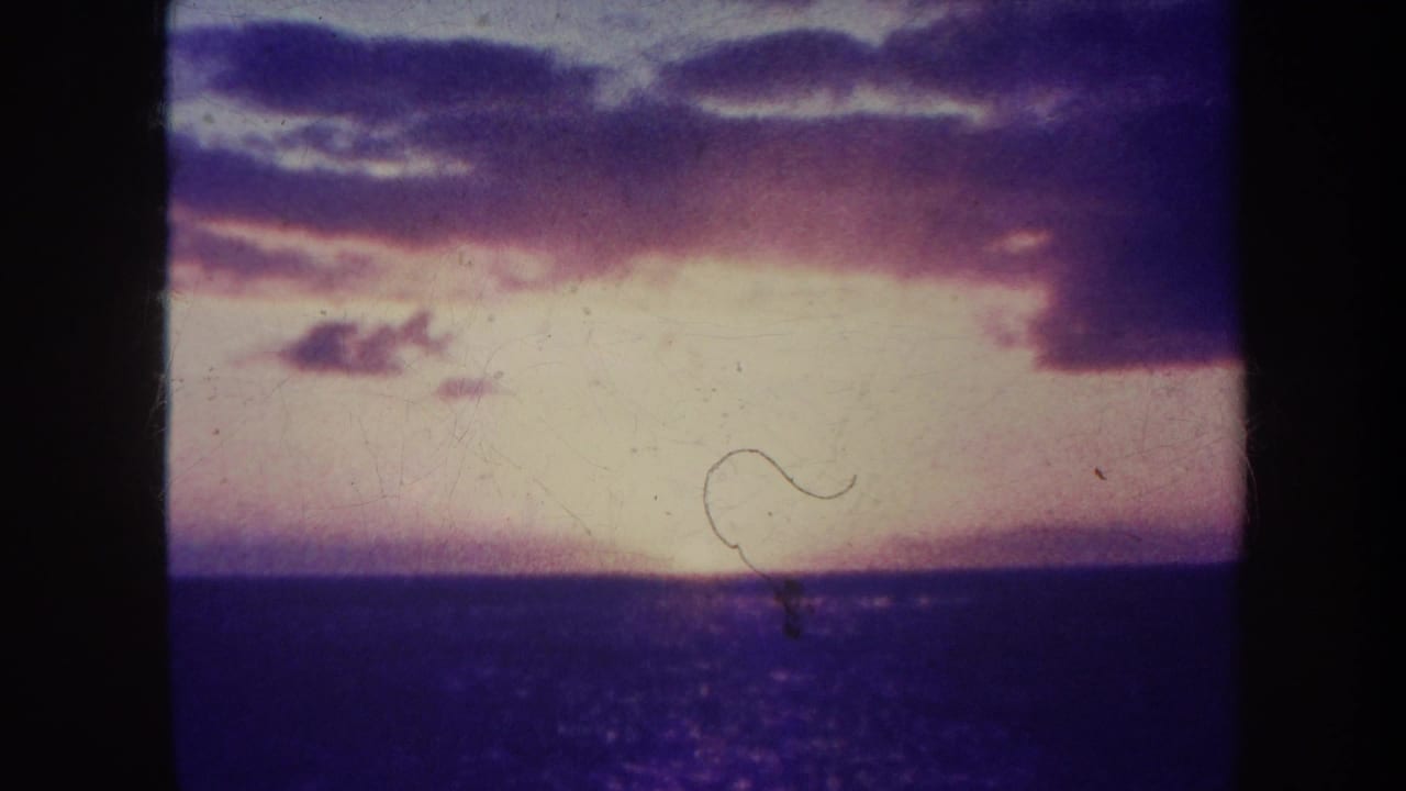Glowing sunset over the ocean with clouds and a visible film hair mark.