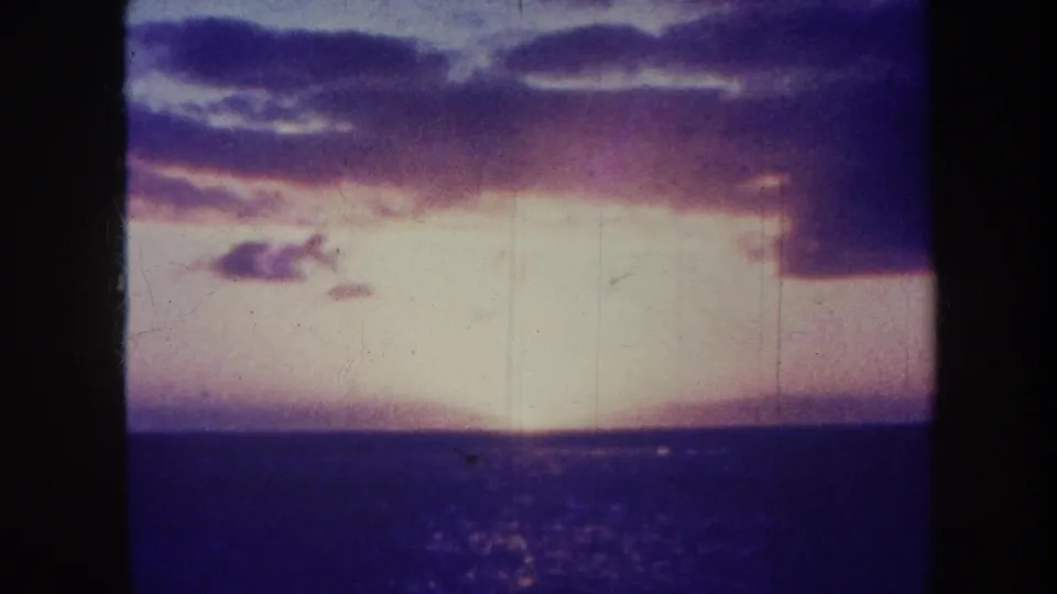 1967 Honolulu 8mm frame showing a low sunset glow, dark sea, faded purple clouds, and vertical film scratches.