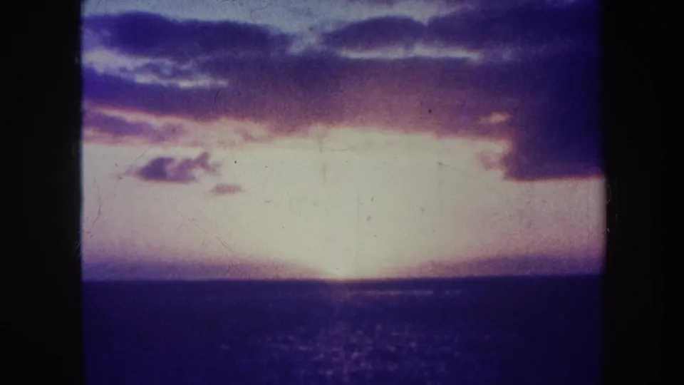 1967 Honolulu 8mm frame showing a bright ocean sunset, calm dark water, purple cloud cover, and soft film grain.