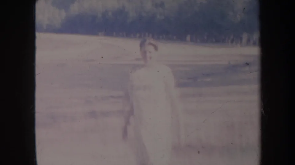 1967 Honolulu 8mm frame with the woman centered in a washed, softly focused outdoor landscape before a distant tree line.