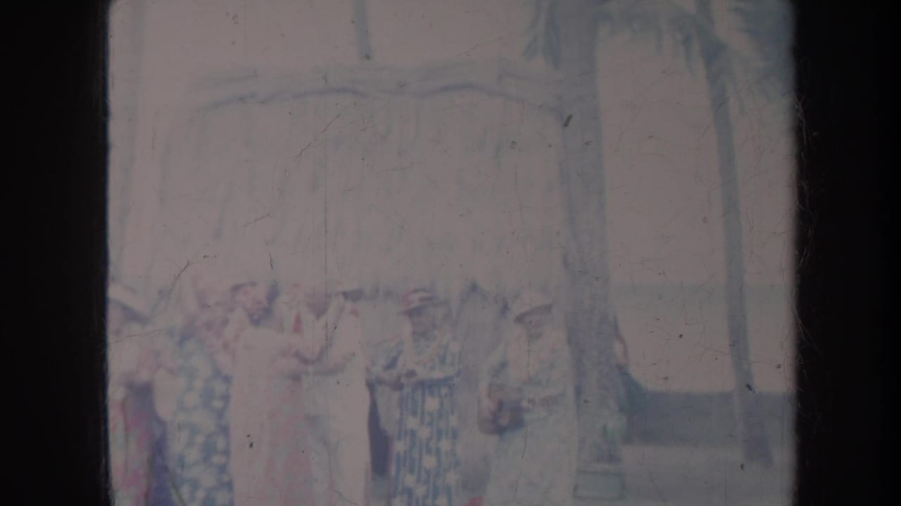 Group of women outdoors, with one figure in white near the center and palm trees behind them.
