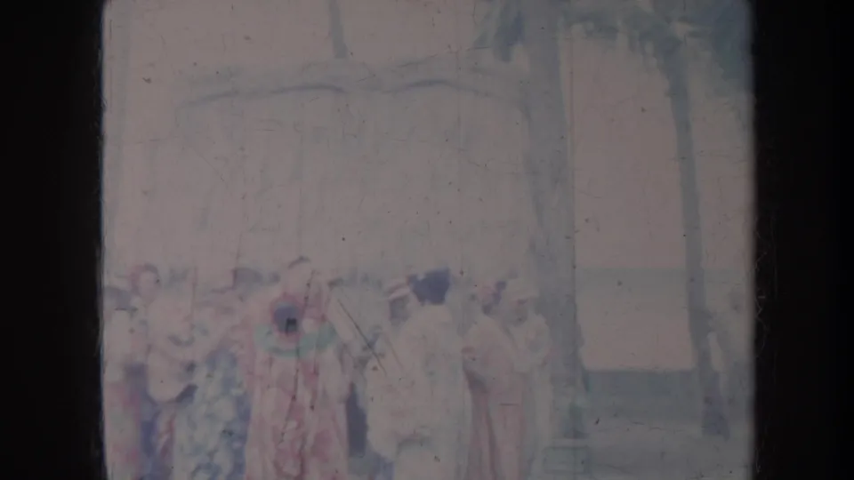 Faded 8mm frame from 1967 Honolulu showing women in colorful gowns near a shaded structure and palm trees.