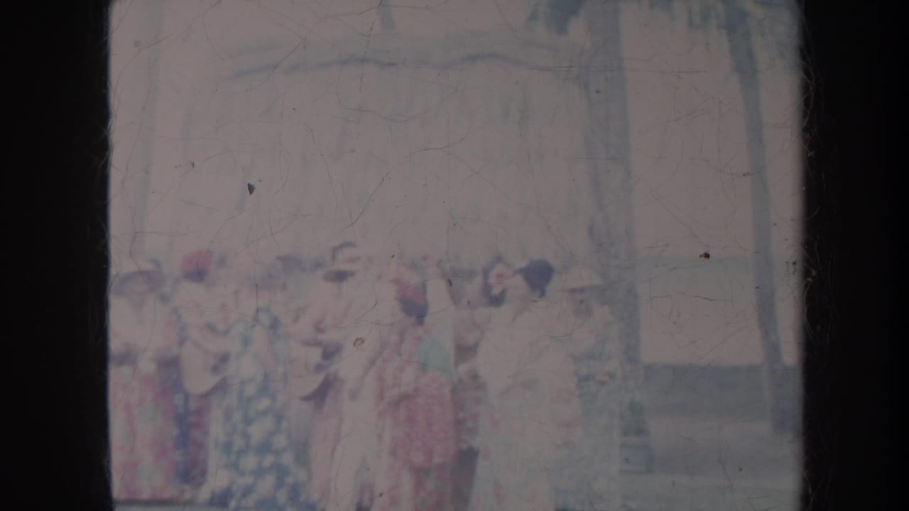 Group of women in dresses standing together outdoors with hats and trees visible.
