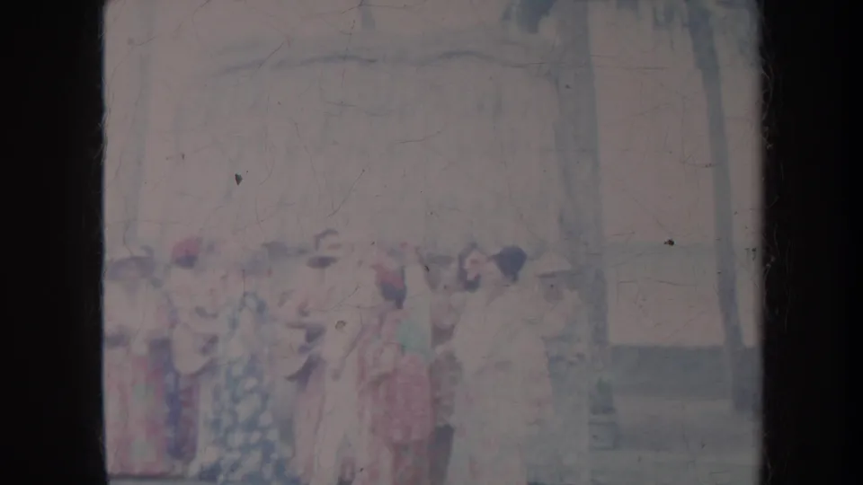 1967 Honolulu frame with women in colorful dresses and hats standing in conversation outside near trees and a pale building.