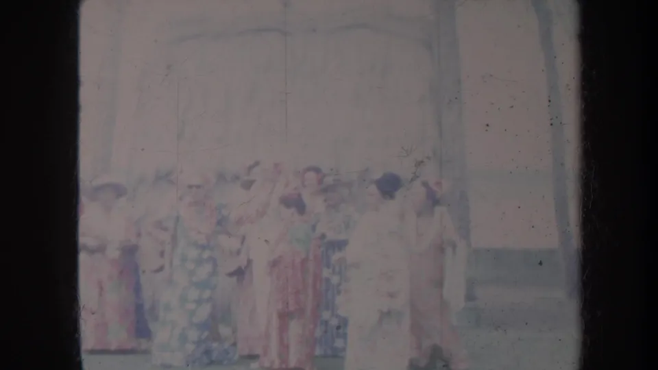 1967 Honolulu home-movie frame of women in dresses and hats gathered outdoors beside a building and trees.