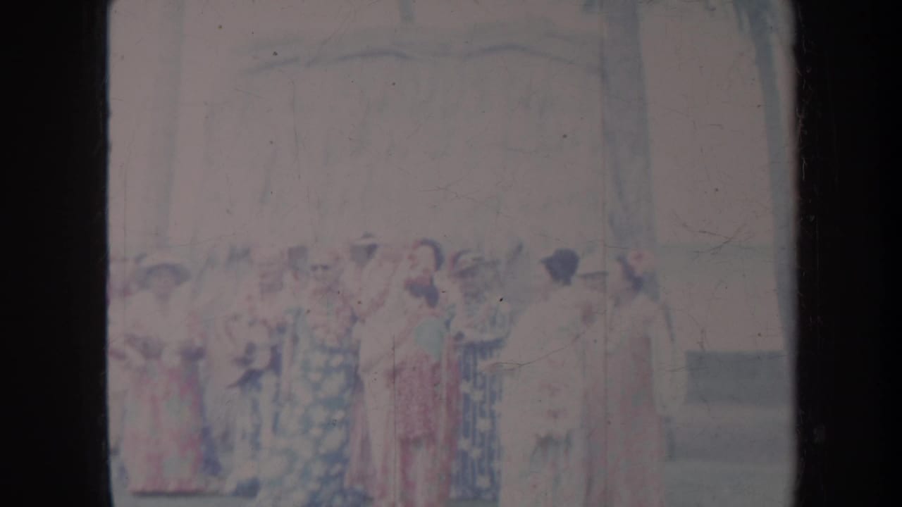 Group of women in colorful long dresses standing outdoors before an audience.