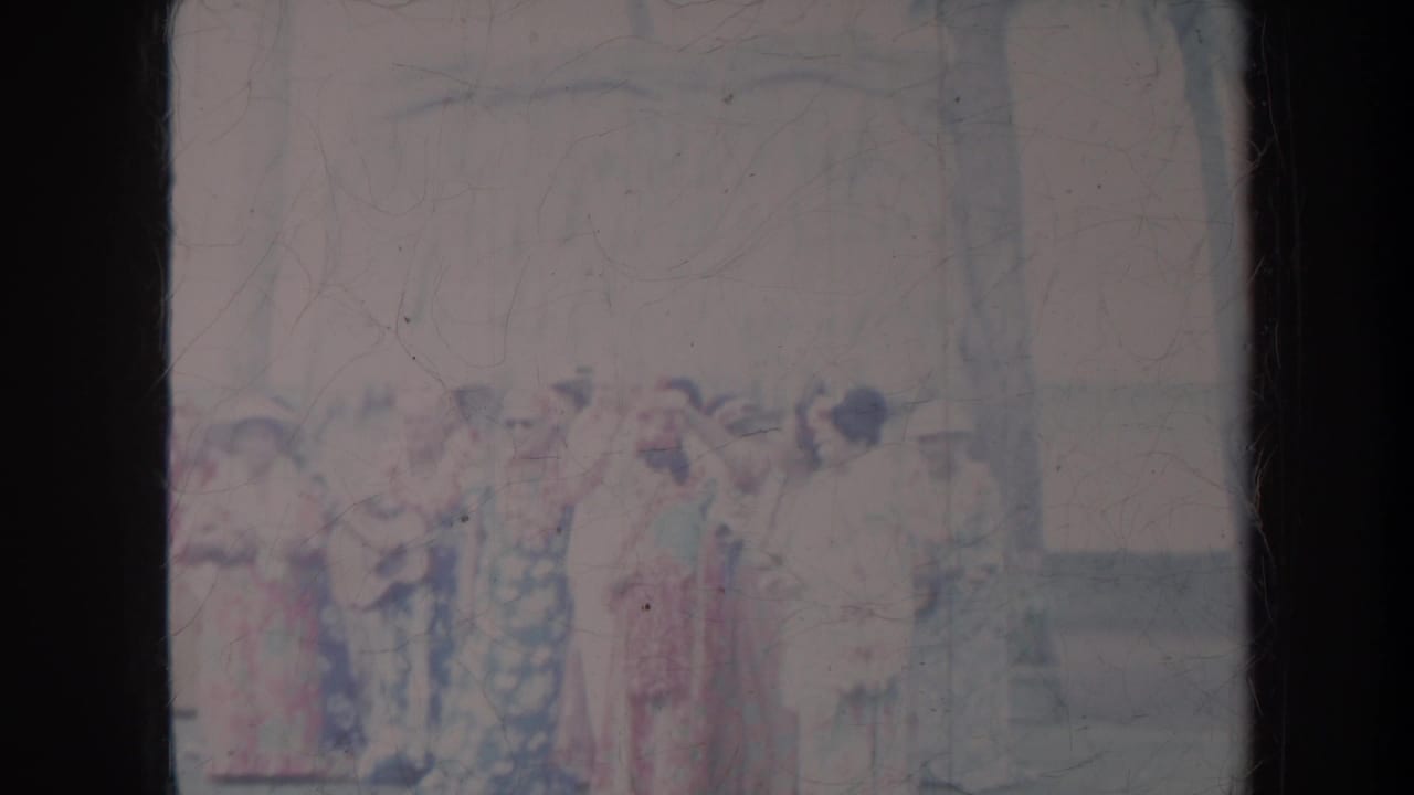 Women in patterned dresses remain grouped outdoors with spectators in the background.