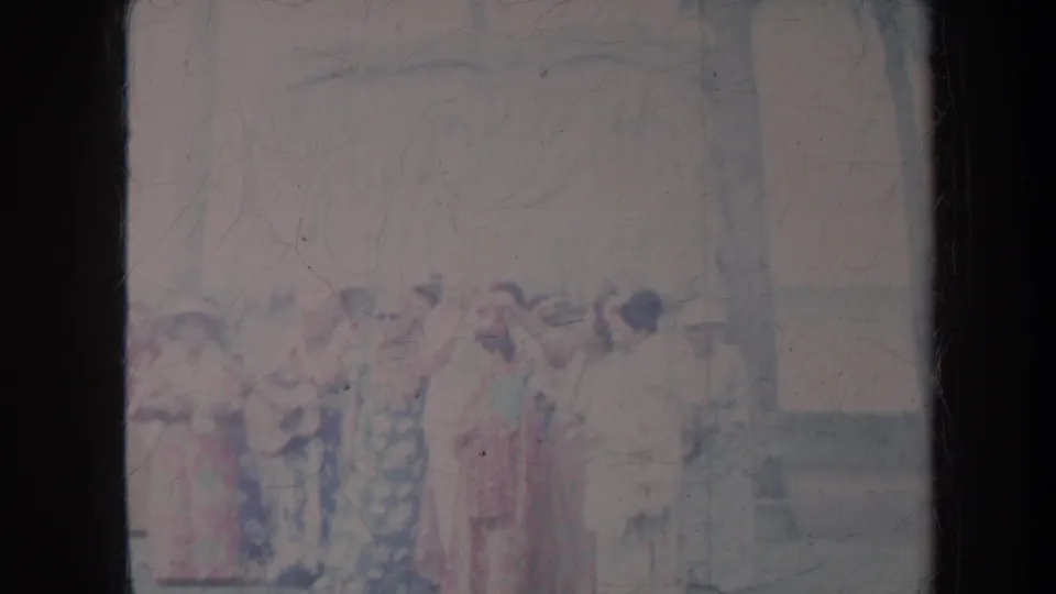 Faded 8mm frame from Honolulu showing a group of women in bright full-length dresses during an outdoor cultural dance moment.