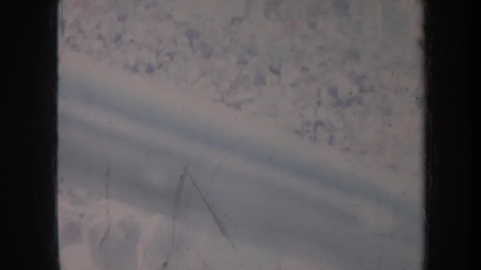 1967 Honolulu home-movie frame showing a distant pale crowd seen through a dark vertical window frame and faded film texture.