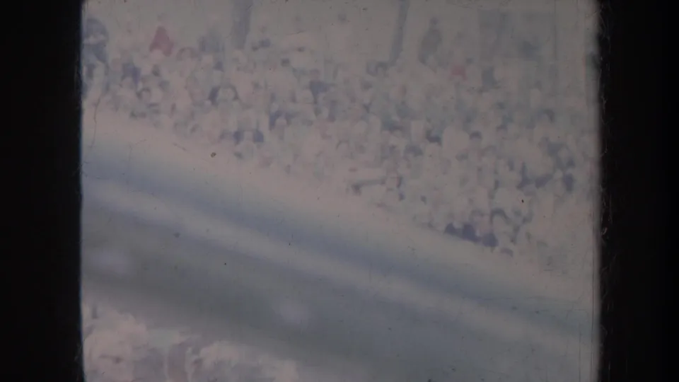 1967 Honolulu 8mm frame with a distant crowd behind dark window framing, grain, scratches, and washed color.