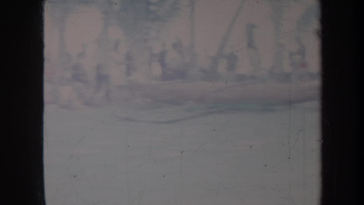 Faded Honolulu home-movie frame with indistinct figures and possible boats near the water, seen through heavy 8mm scan borders.