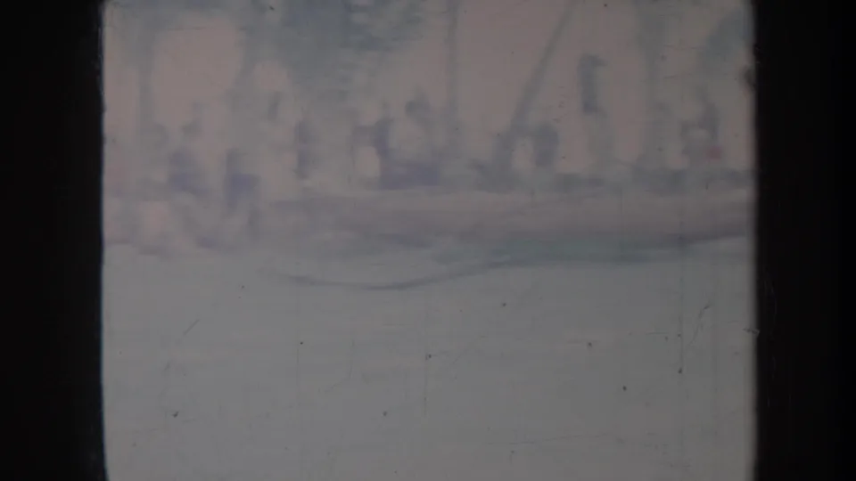 Faded Honolulu home-movie frame with indistinct figures and possible boats near the water, seen through heavy 8mm scan borders.