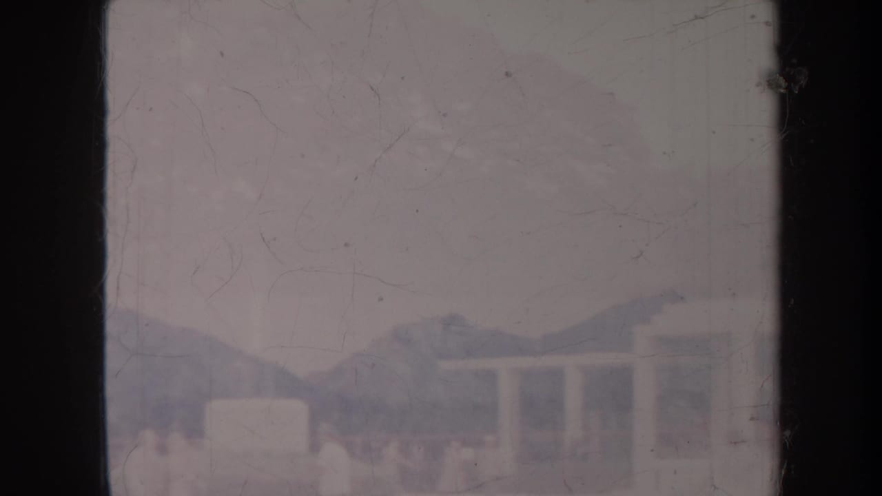 Distant white structure and mountain ridge seen through scratched film gate edges.
