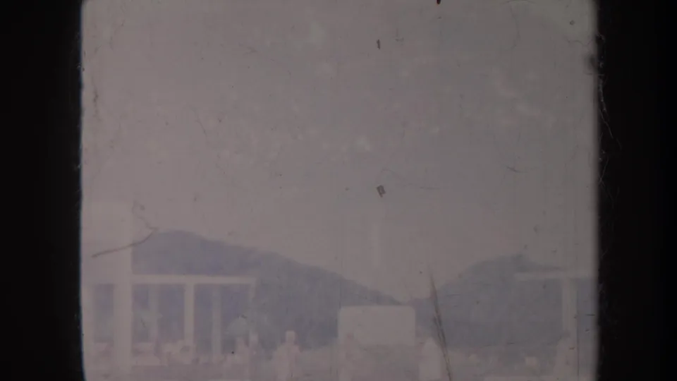 Distant Honolulu building and mountain backdrop in a faded 1967 8mm frame with dust and scratches.