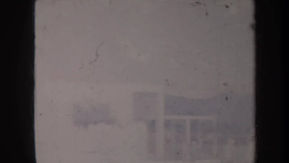 Faded Honolulu 8mm frame showing a distant low building, mountain ridge, scratches, and washed-out color.
