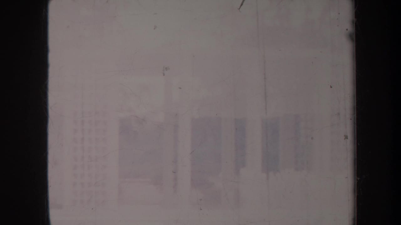 Faded view of a pale building and courtyard partly obscured by dark film borders.