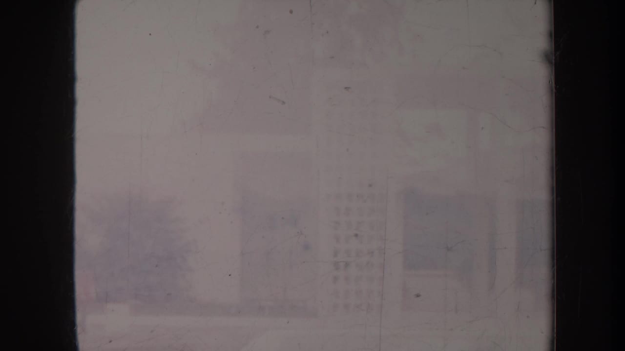 Faint exterior courtyard view with a building, hedge, and walkway behind film fading.