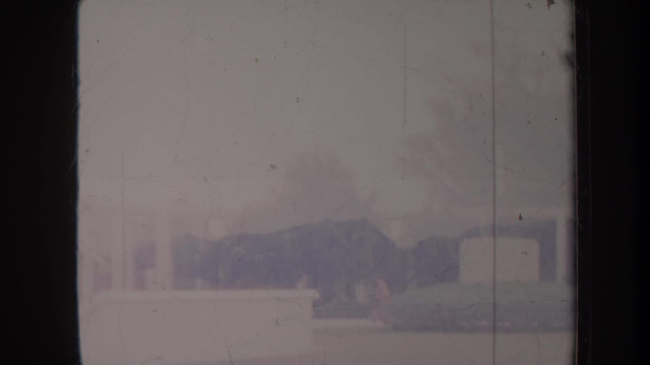 Washed-out view of a pale building facade and low wall behind dark film borders.