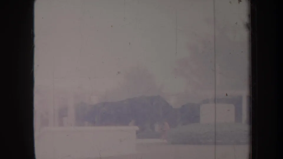 Faded 1967 Honolulu 8mm frame showing a distant building facade, low wall, and hazy grounds through scratched film.