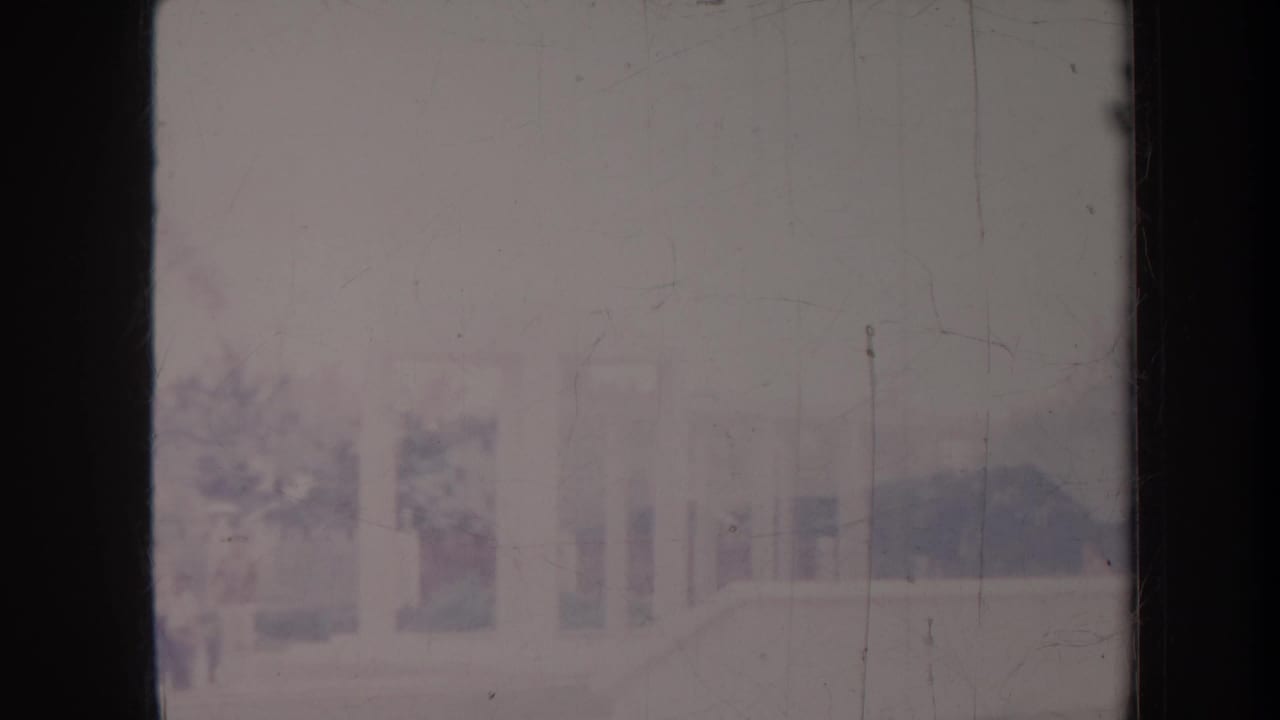 Pale columned structure and landscaped area seen through a faded, scratched frame.