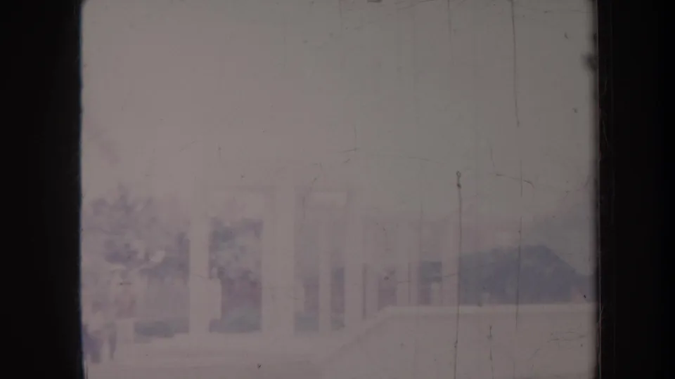 Washed-out Honolulu home-movie frame with pale columns, building edges, and indistinct landscaping in soft focus.